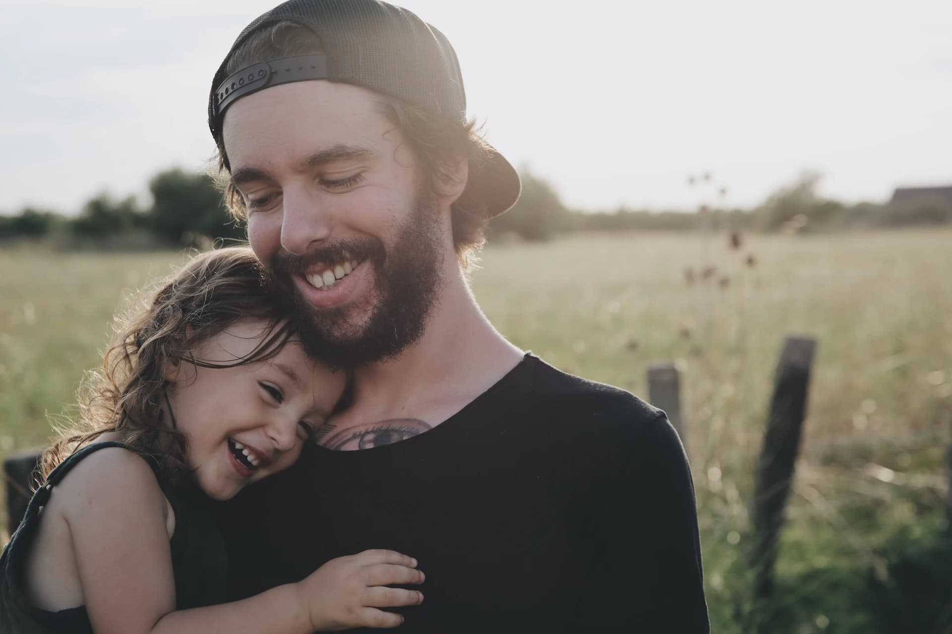 Pai sorrindo enquanto abraça a filha ao ar livre